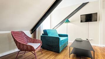 Una sala de estar moderna con techo inclinado, un sofá color turquesa, un sillón de mimbre rojo y una mesa de centro negra.