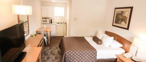 Habitación de hotel con cama, mesita de noche, televisión, kitchenette y un cuadro en la pared.