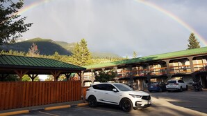 A parking area with a white SUV, a building with a green roof, and a mountain backdrop. - Crystal Springs Lodge (Radium Hot Springs)