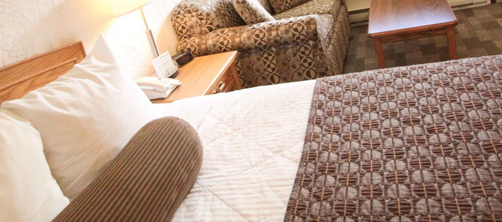 Ein Bett mit einem gemusterten Überwurf, einem hölzernen Kopfteil und einem Kopfkissen.