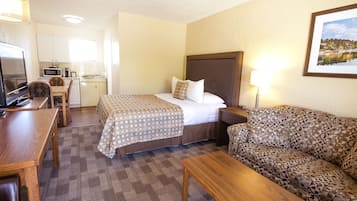 Una camera d'albergo con un letto, un divano, una scrivania, una televisione, un angolo cottura e un quadro appeso al muro.