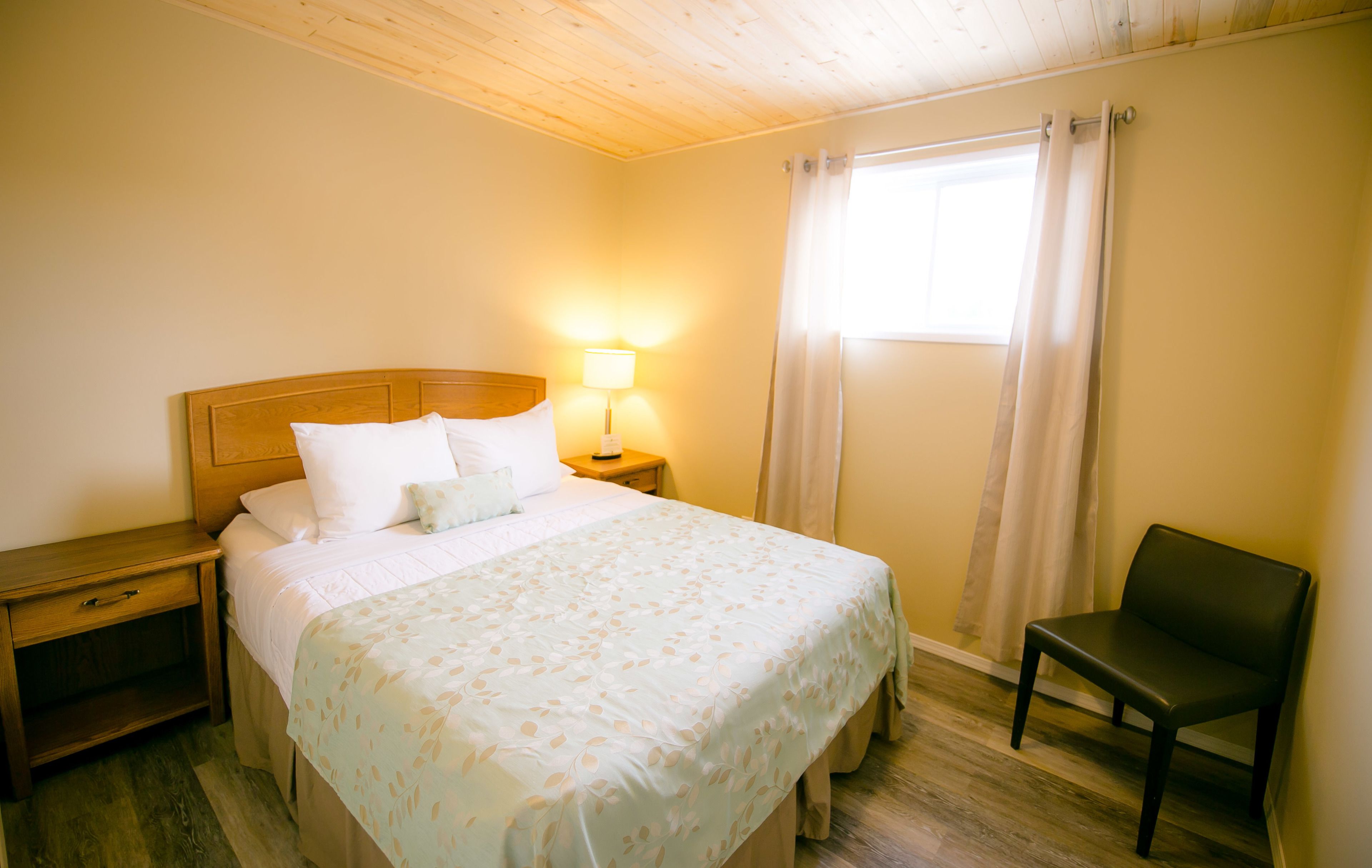A neatly made bed with a floral bedspread, a bedside lamp, a wooden nightstand, and a chair.
