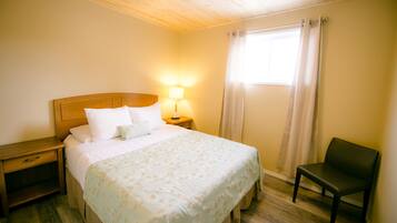 A neatly made bed with a floral bedspread, a bedside lamp, a wooden nightstand, and a chair.