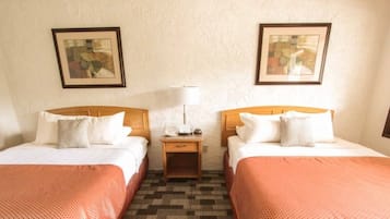 A hotel room with two single beds, a nightstand with a lamp, and two framed pictures on the wall.