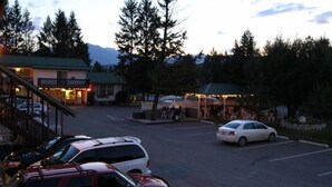A parking lot with several cars, a building with a green roof, and a dining area with outdoor seating. - Crystal Springs Lodge (Radium Hot Springs)