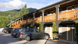 A hotel with multiple balconies, a parking lot, and a mountainous backdrop. - Crystal Springs Lodge (Radium Hot Springs)