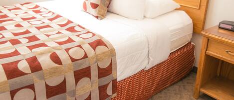 A hotel room with a bed, a wooden headboard, a nightstand, and a red and white patterned bedspread.