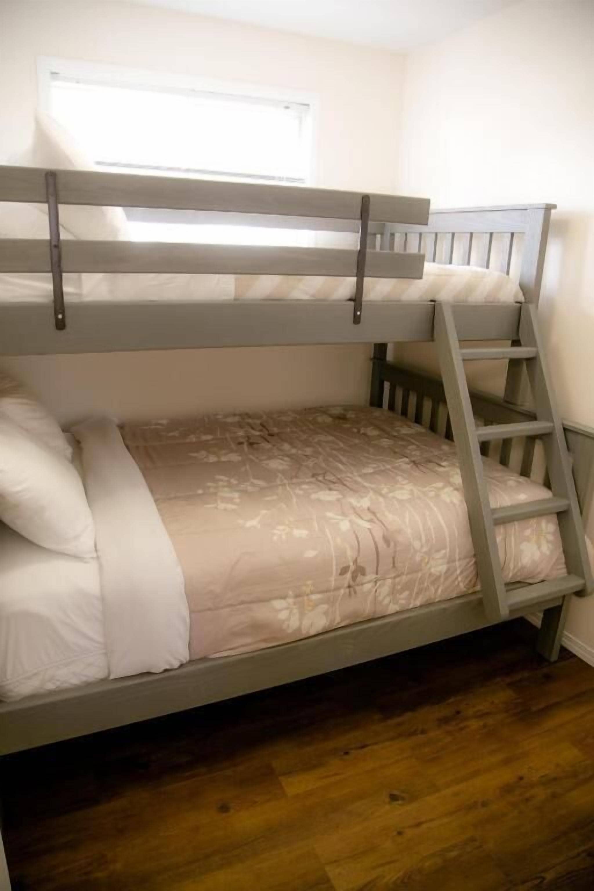 A bunk bed with a ladder, a window above, and a wooden floor.