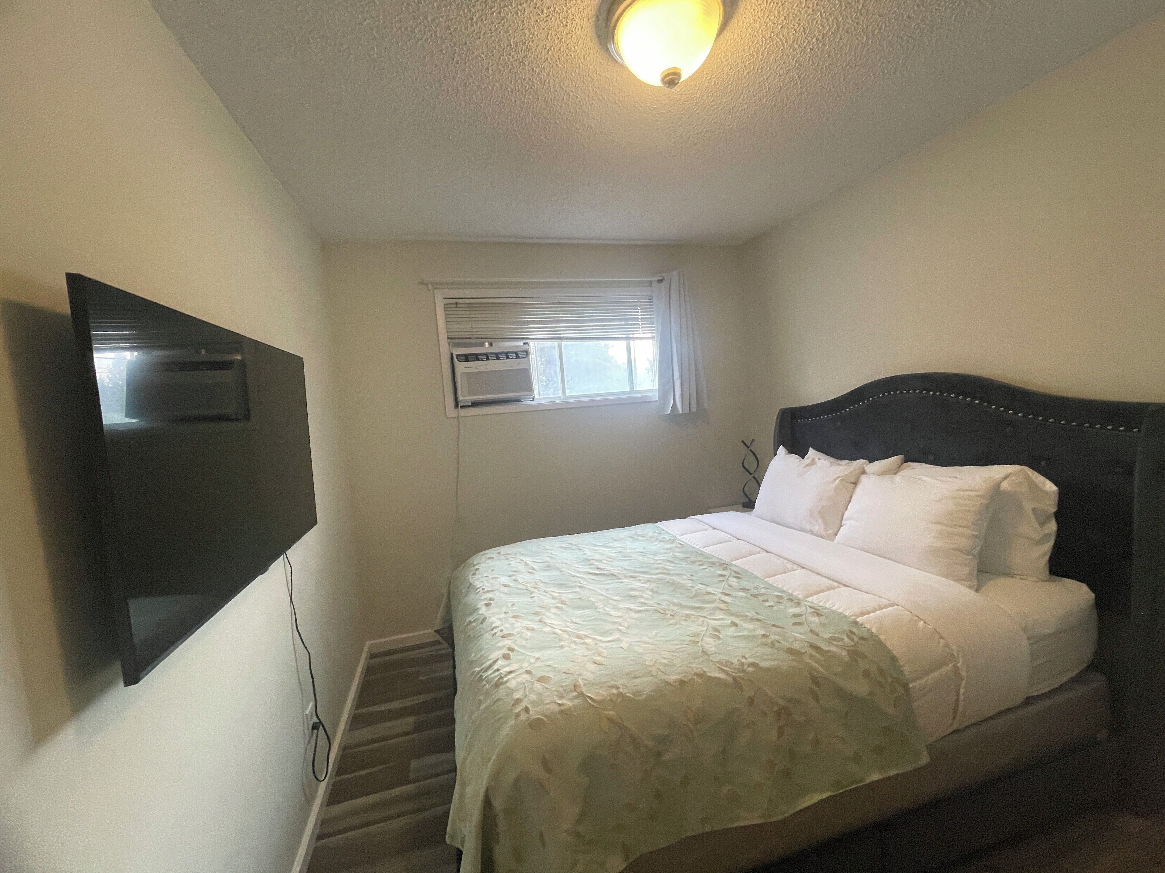 A bedroom with a bed, a television mounted on the wall, and an air conditioning unit.