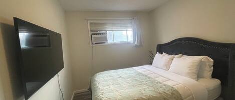 A bedroom with a bed, a television mounted on the wall, and an air conditioning unit.