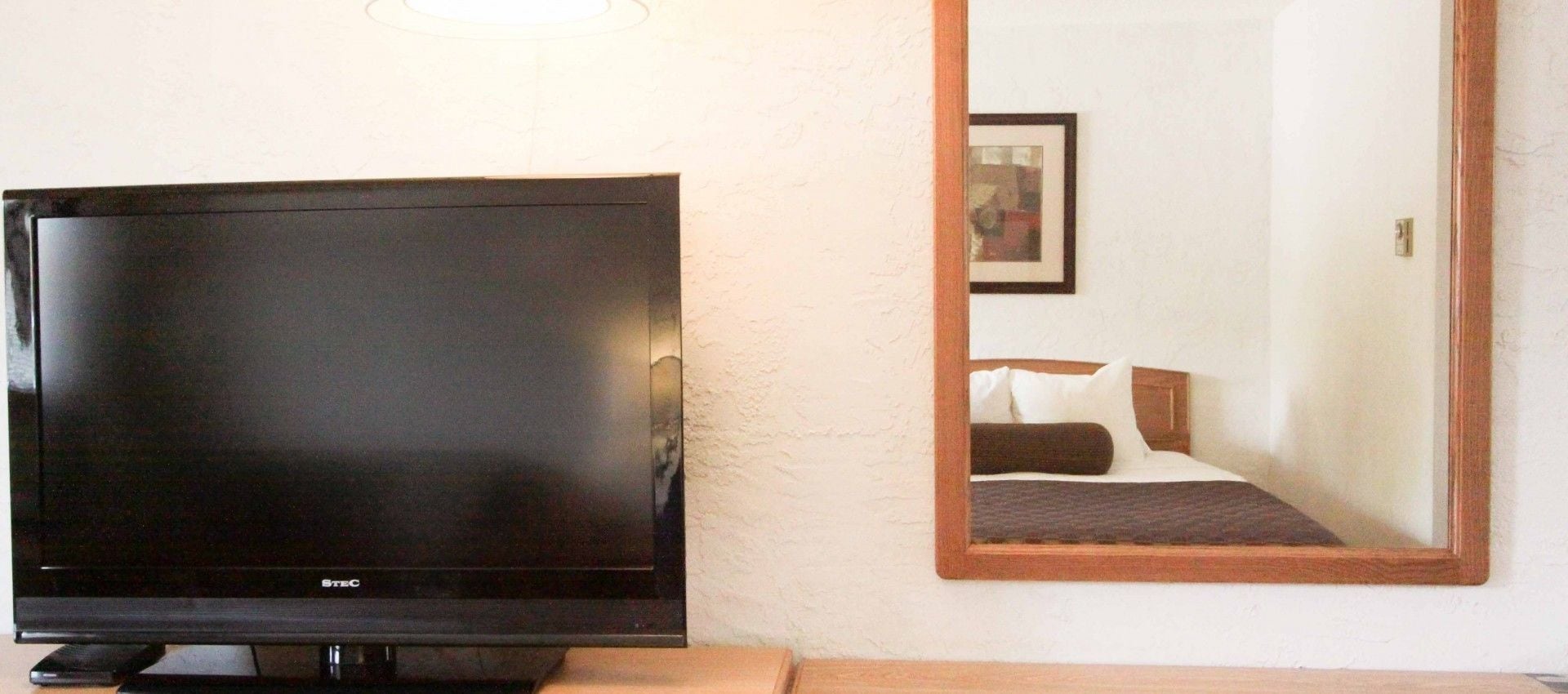 A television on a stand, a bed with pillows, and a mirror on the wall.