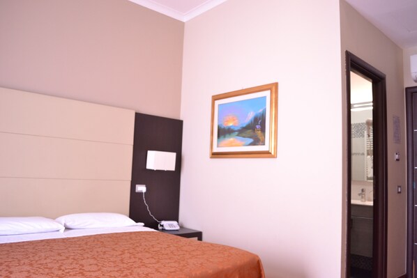 A hotel room with a bed, a nightstand, a painting on the wall, and a door leading to a bathroom.
