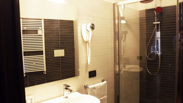 A bathroom with a sink, mirror, towel rack, and a glass-enclosed shower area.