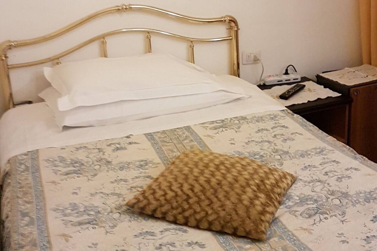 A neatly made bed with a floral bedspread and a single brown pillow.