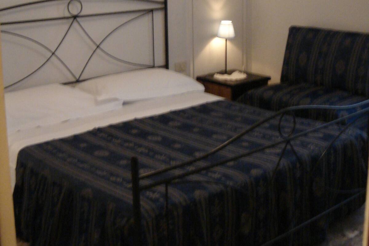 A bedroom with a single bed, a nightstand, a lamp, and two framed pictures on the wall.