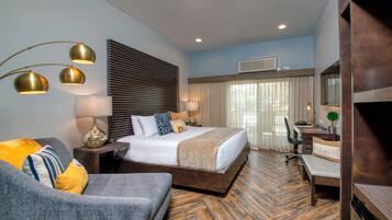 A hotel room with a bed, a desk, a chair, a sofa, and a lamp.
