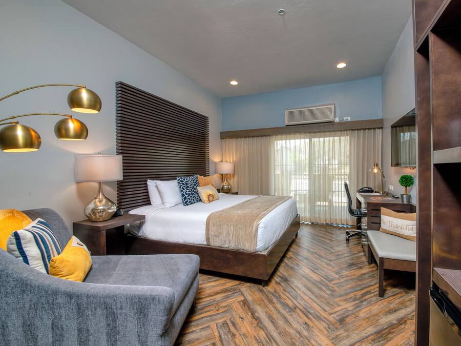 A hotel room with a bed, a desk, a chair, a sofa, and a lamp.