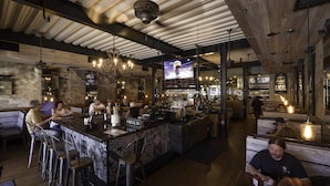 A bar area with a check-in counter, seating, and a television screen displaying a sports event.