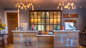 A reception desk with two staff members, a wooden reception desk, a 'WELCOME' sign, and a window with a view.