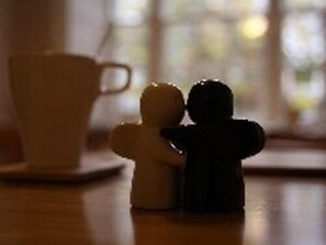 A small figurine of a person holding another, placed on a wooden surface next to a white cup. - Angel Guest House (Tiverton)