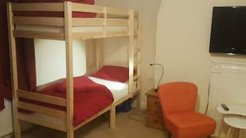 Una cama litera con ropa de cama roja, una mesita de noche de madera, una silla naranja y una pequeña mesa blanca con un control remoto.