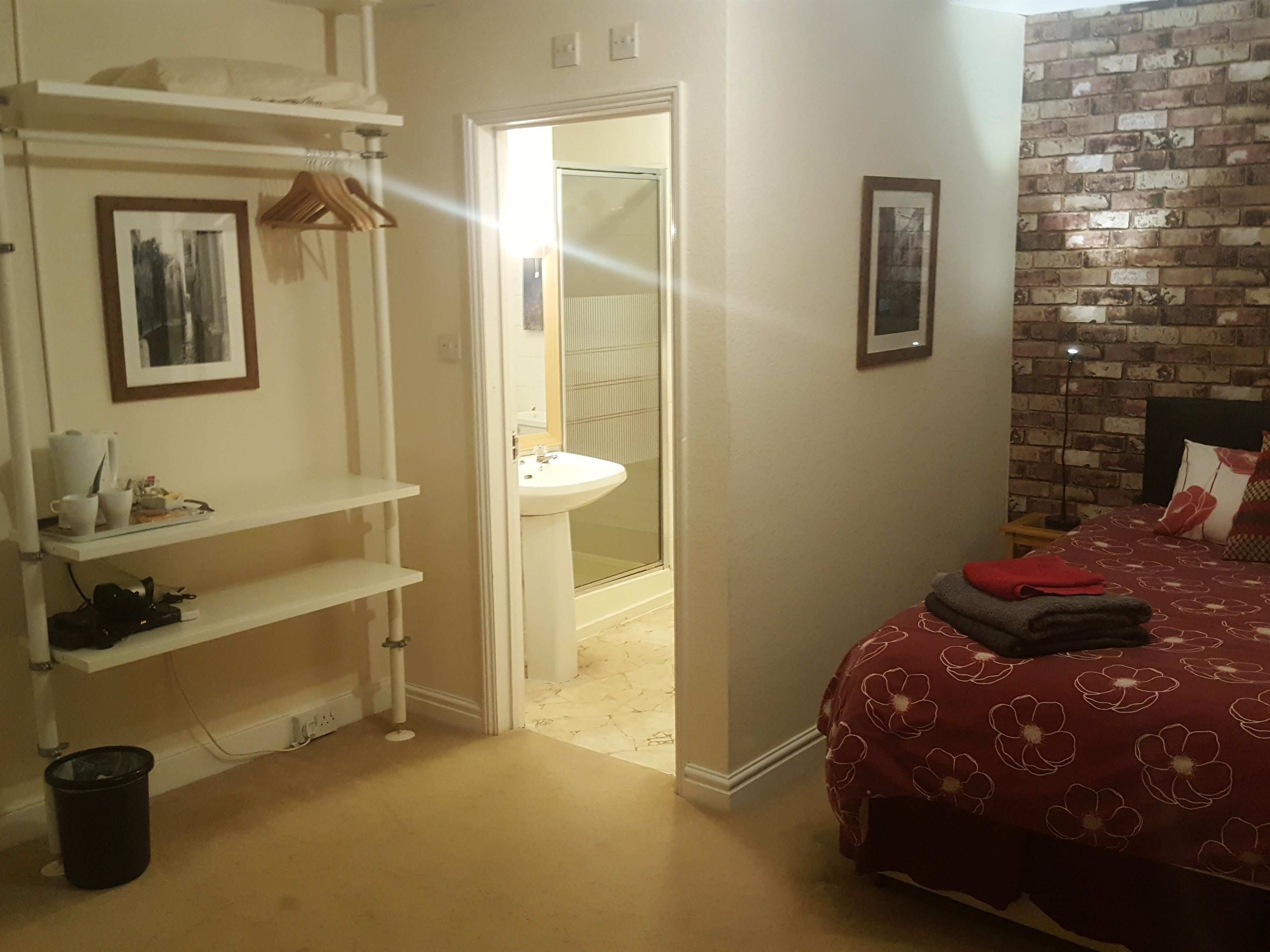 A bedroom with a red floral bedspread, a white sink, a mirror, and a brick wall.