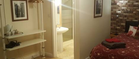 A bedroom with a red floral bedspread, a white sink, a mirror, and a brick wall.