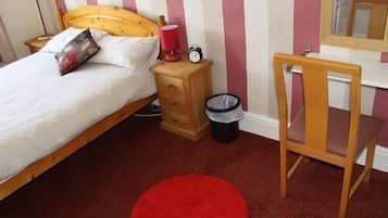 Une chambre à coucher avec un lit, une table de chevet en bois, une poubelle rouge, une chaise en bois et un miroir accroché au mur.