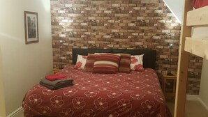 Un dormitorio con pared de ladrillo, cama con colcha floral roja y una lámpara de noche.
