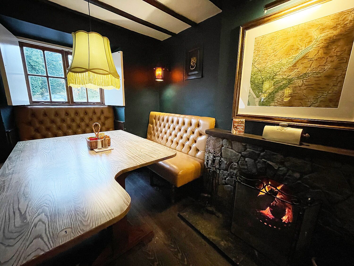 A cozy room with a wooden table, a cushioned bench, a fireplace, and a map on the wall.