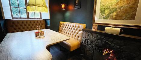 A cozy room with a wooden table, a cushioned bench, a fireplace, and a map on the wall.