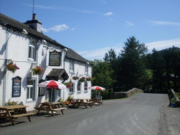 A white building with a sign reading "Bridge Inn" and outdoor seating with umbrellas.