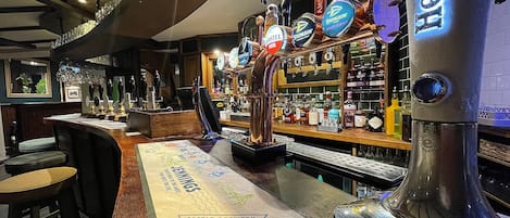A bar area with multiple taps, a counter with various bottles, and stools.