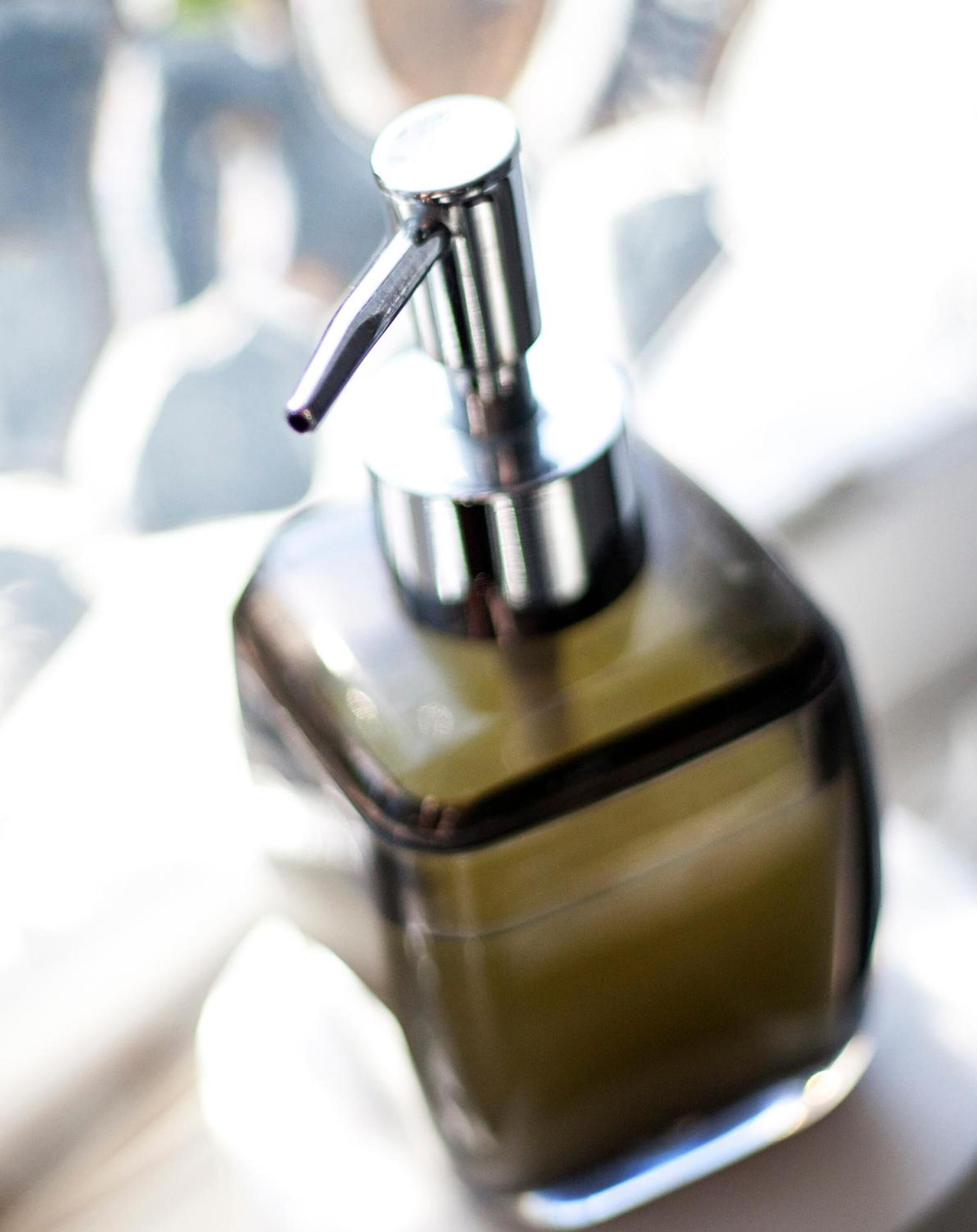 A bottle with a pump dispenser, likely containing a liquid product, placed on a reflective surface.