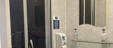 A modern bathroom with a glass shower door, a sink with two faucets, a mirror, and a soap dispenser on the wall.