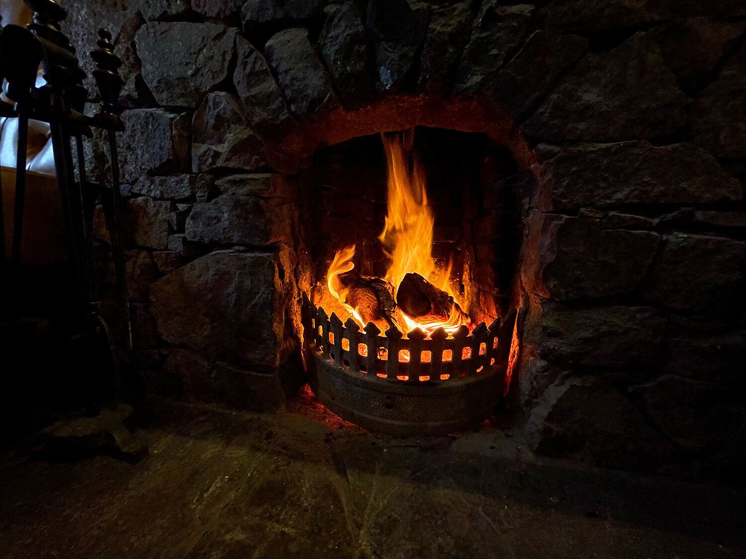 A stone fireplace with a metal fire screen, burning logs, and a visible chimney.