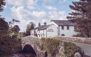 Un edificio blanco con un letrero que dice "Bridge Inn" cruzando un puente de piedra.