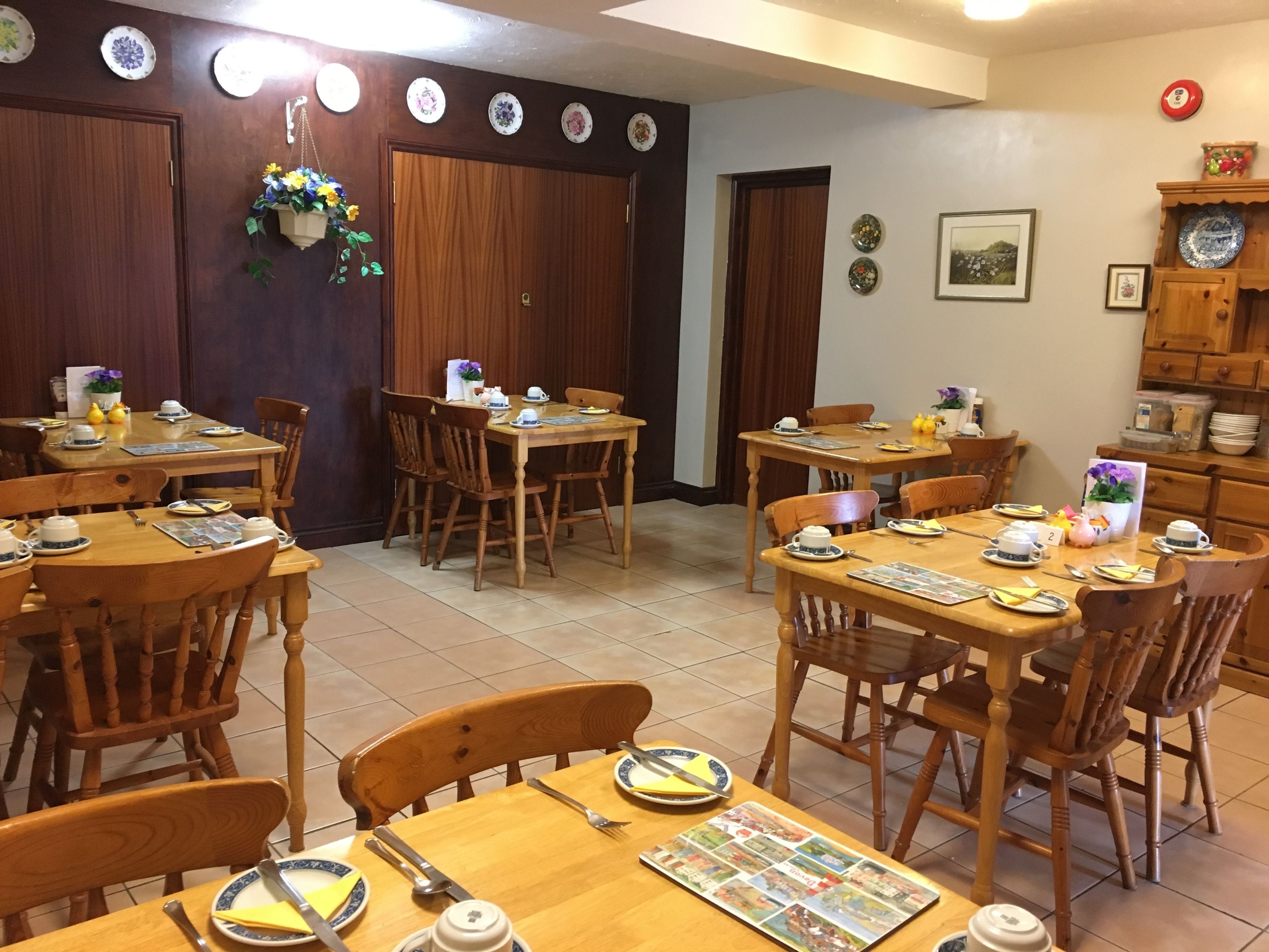 A dining area with wooden tables and chairs, surrounded by walls decorated with plates and a framed picture.