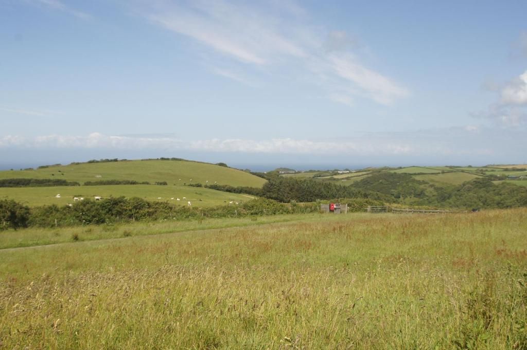 Ländliche Landschaft mit sanften Hügeln, einem eingezäunten Bereich und einer kleinen roten Struktur.