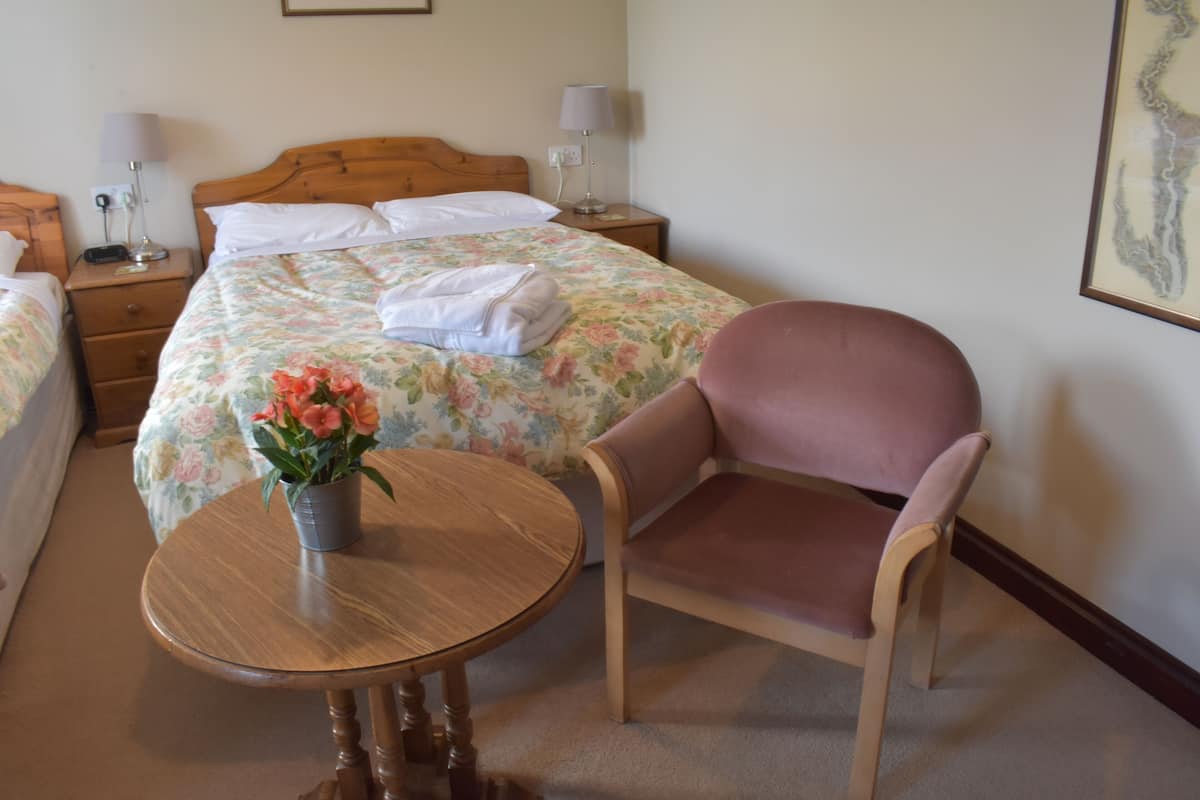 A hotel room with a bed, bedside tables, a chair, a small table, and a vase with flowers.