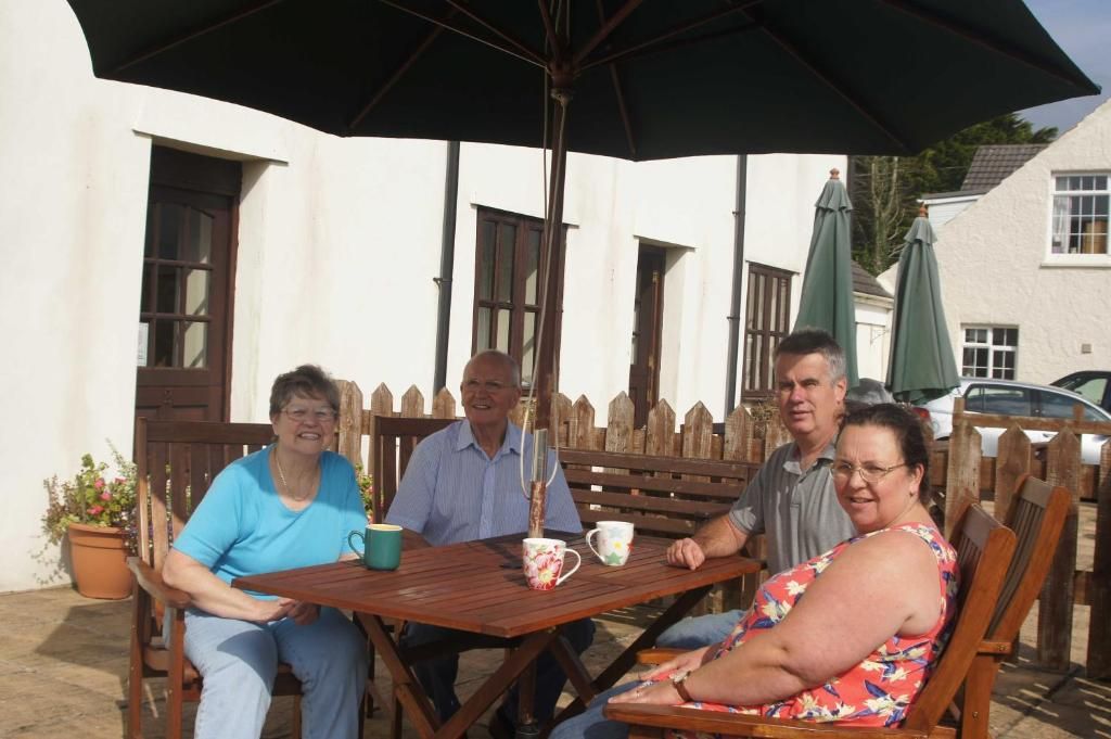 A group of people seated at an outdoor wooden table with a black umbrella overhead.