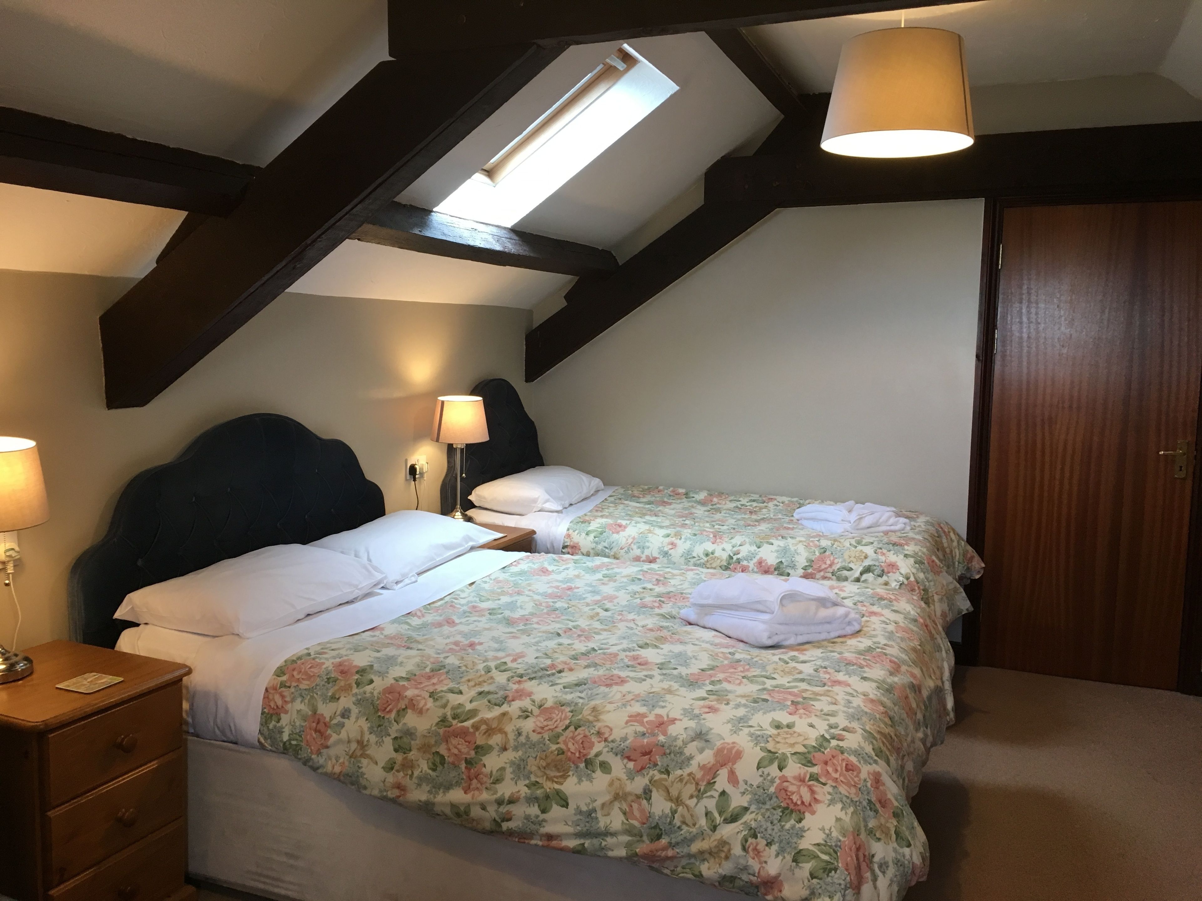 Une chambre avec deux lits, une lucarne, des poutres en bois et une porte en bois.