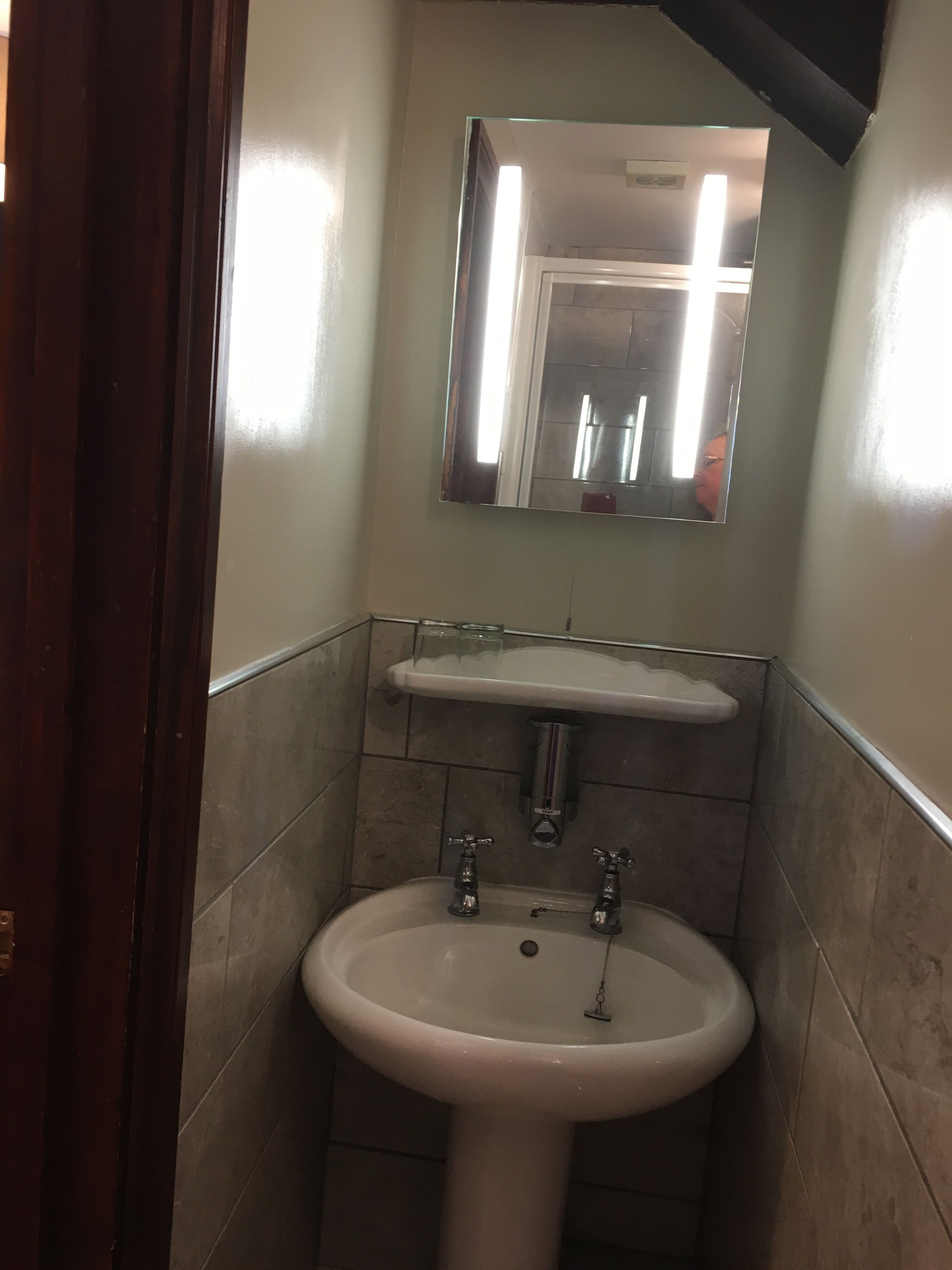 A bathroom with a white sink, a mirror above it, and a wooden door frame.