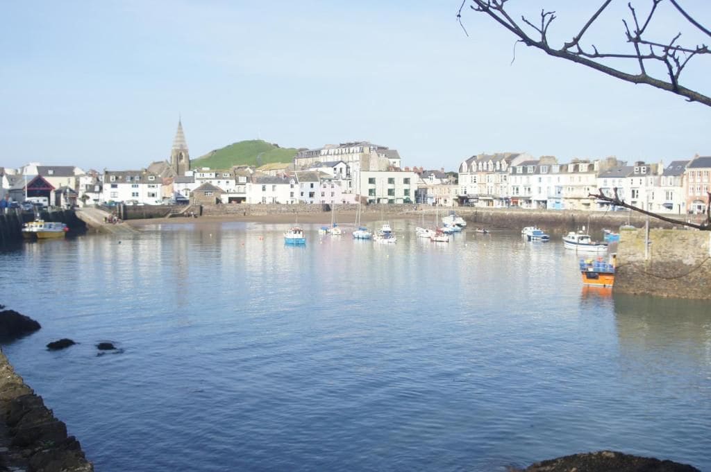 A coastal town with a calm harbor, buildings along the shore, and a prominent church spire.