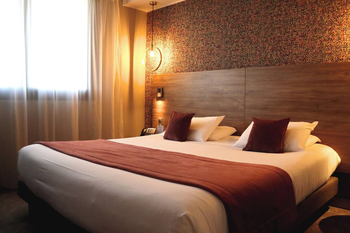 A hotel room with a large bed, a wooden headboard, a telephone, and a nightstand with a lamp.