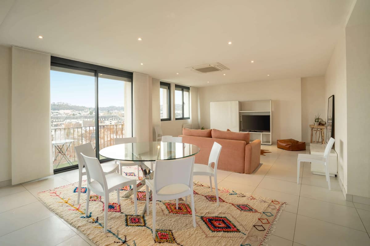 A modern living room with a glass dining table, white chairs, a pink sofa, and a TV stand.