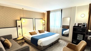 A hotel room with a bed, a sofa, a chair, a desk, and a mirror.