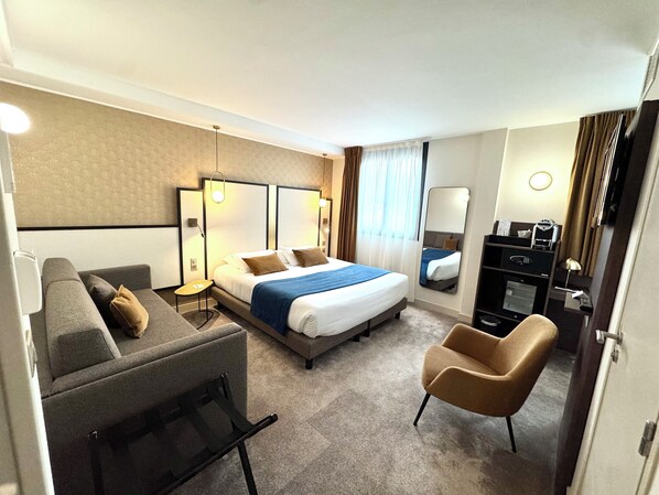 A hotel room with a bed, a sofa, a chair, a desk, and a mirror.