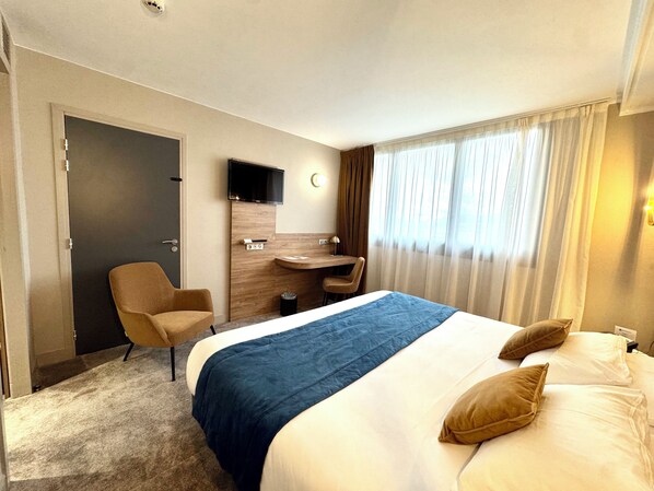 A hotel room with a bed, a desk, a chair, a TV, and a window with curtains.