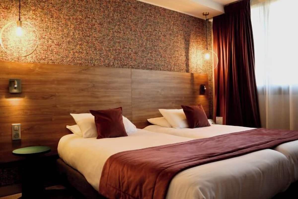 A hotel room with a large bed, two bedside tables, a wooden headboard, and a patterned wall.